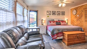 Une chambre à coucher comprenant un lit, une commode en bois, un canapé en cuir, une table de chevet et un ventilateur de plafond.