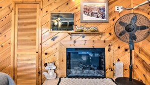 Un intérieur en bois avec une cheminée, un panneau d’accueil encadré, un ventilateur et un animal en peluche.
