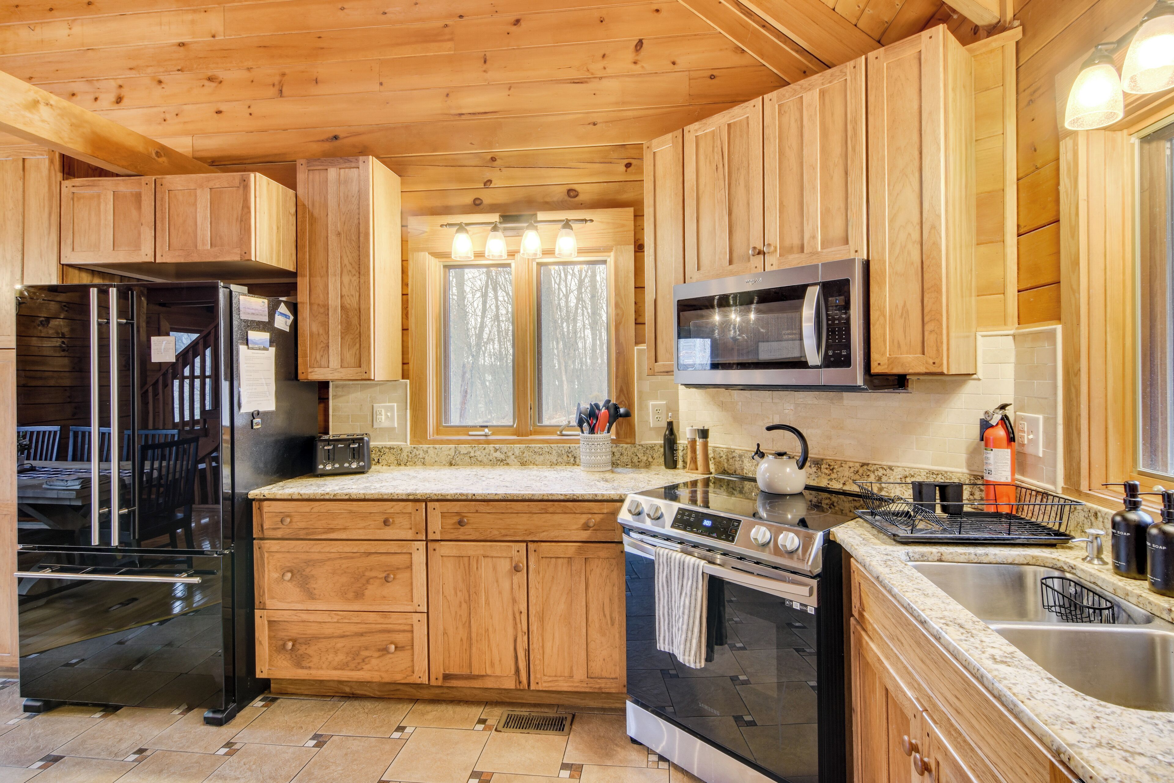 Une cuisine avec des meubles de rangement en bois, un réfrigérateur noir, un four à micro-ondes, un four traditionnel et un évier.