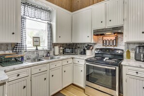 Una cocina con armarios blancos, microondas, estufa y lavaplatos.