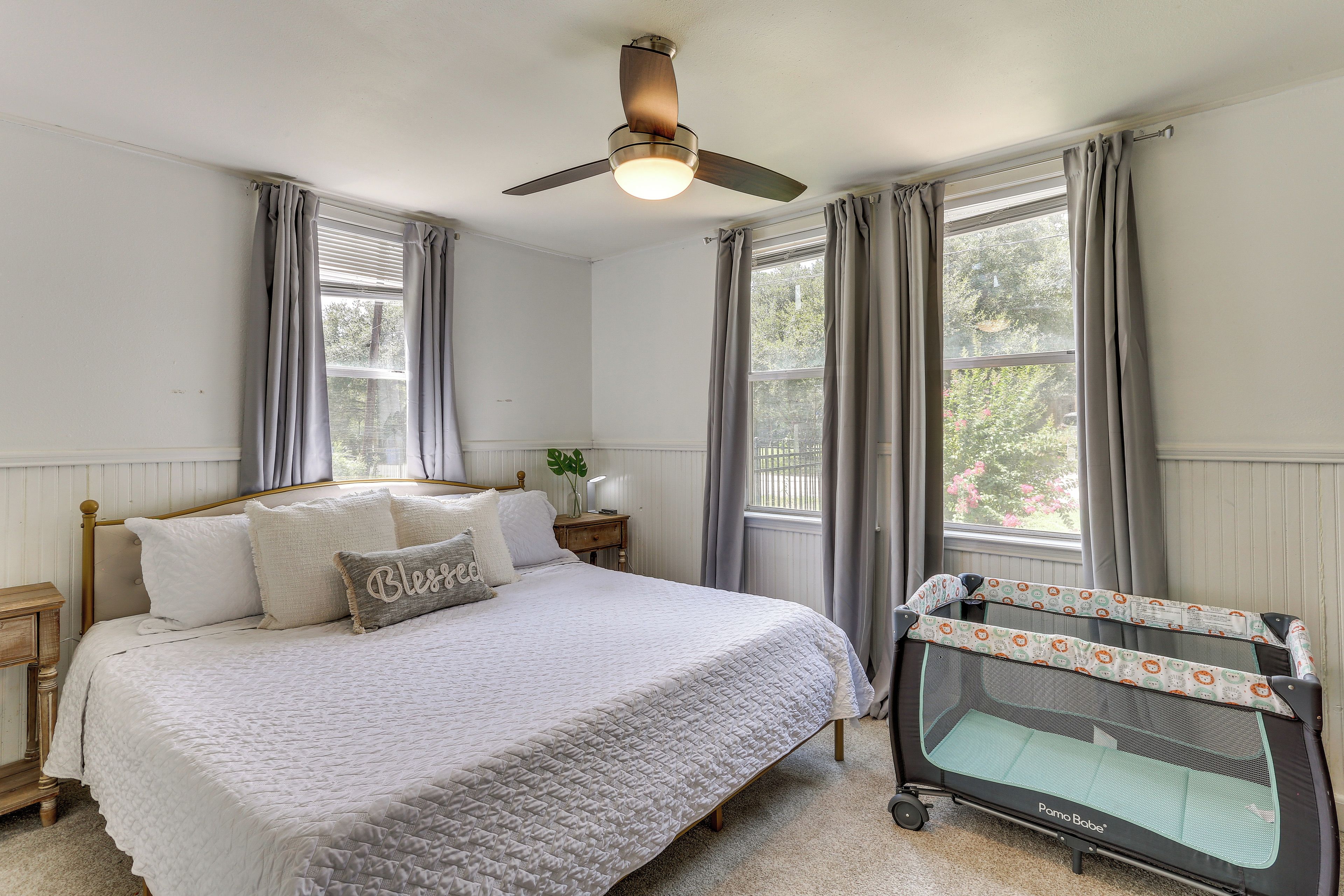 Une chambre à coucher avec un lit, une table de chevet, un ventilateur de plafond et une fenêtre avec des rideaux.
