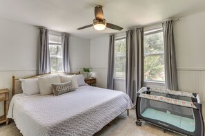 Un dormitorio con cama, mesita de noche, ventilador de techo y ventana con cortinas.