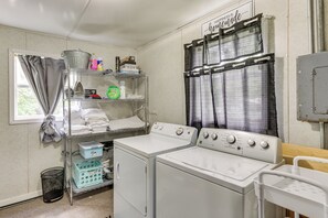 Un lavadero con lavadora, secadora y estantes con productos de limpieza.