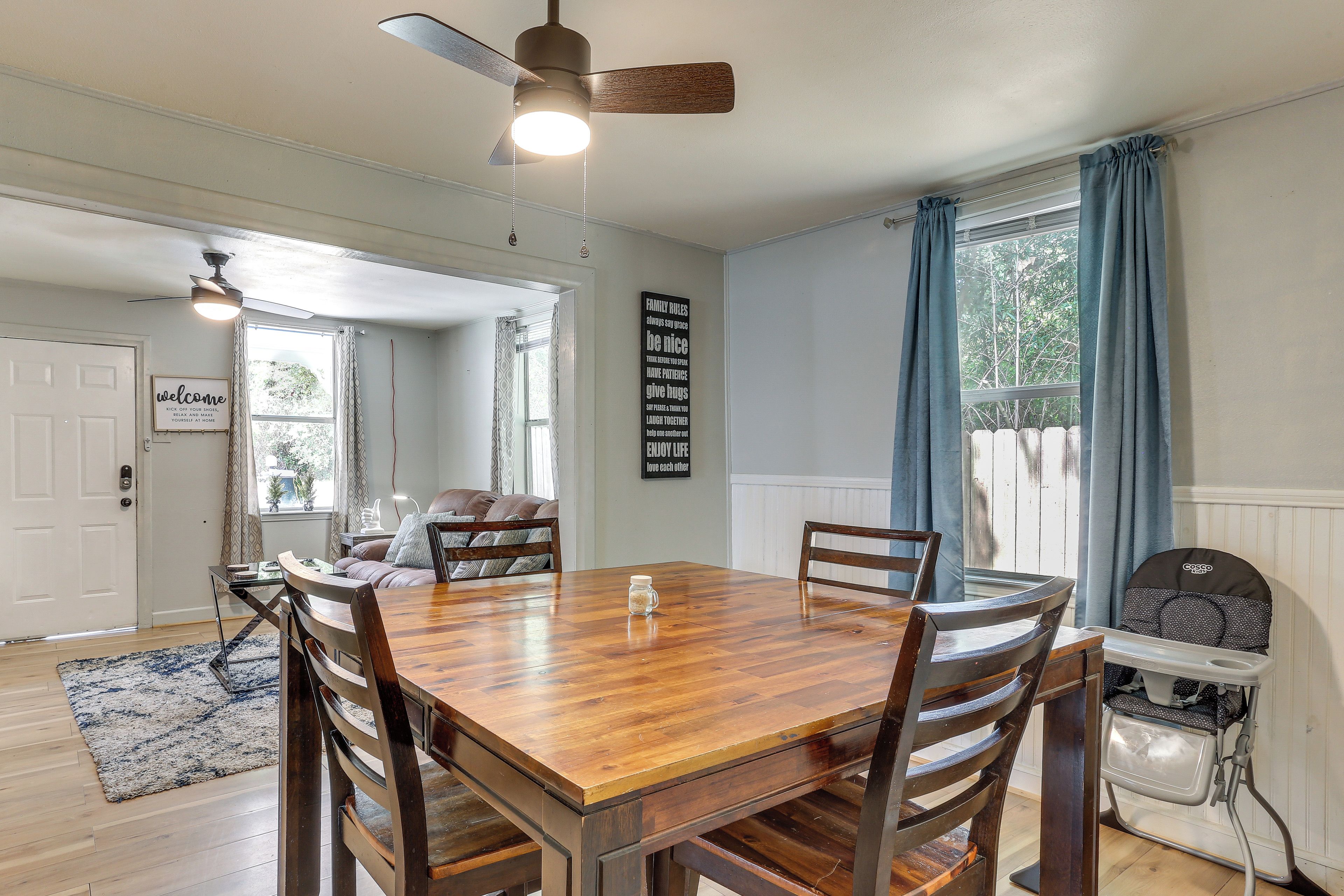 Un coin repas avec une table et des chaises en bois, un ventilateur de plafond et une vue sur l’extérieur par une fenêtre agrémentée de rideaux.