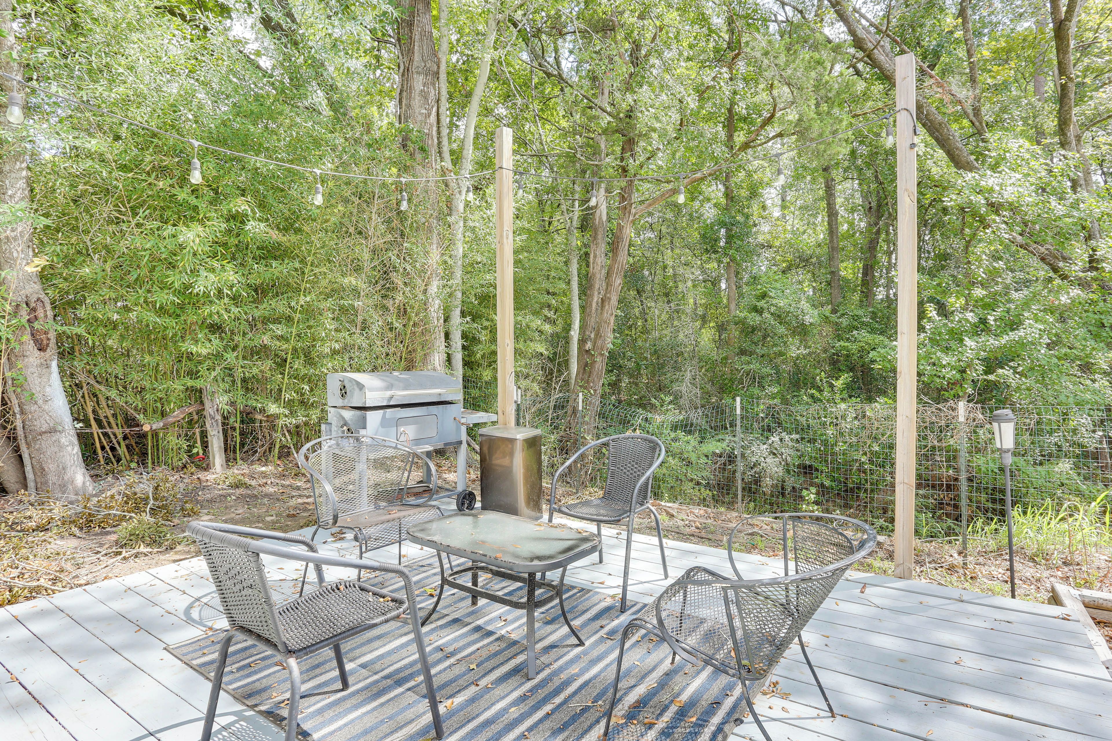 An outdoor deck with metal chairs and a grill, surrounded by trees.
