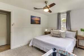 A bedroom with a bed, a nightstand, a ceiling fan, a window with curtains, and a wall-mounted painting.