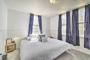 Un dormitorio ordenado con una cama grande, una mesita de noche con una lámpara, y una pequeña mesita de madera con un marco de fotos.