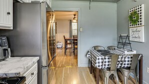 Cocina compacta con refrigerador, microondas y armarios de madera. Se observa un comedor con una mesa y sillas a cuadros a través de un umbral abierto.