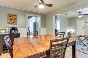 A dining area with a wooden table and chairs, a ceiling fan, and a kitchen visible through an open door.