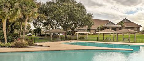 A swimming pool with a surrounding deck, palm trees, and a gazebo structure.