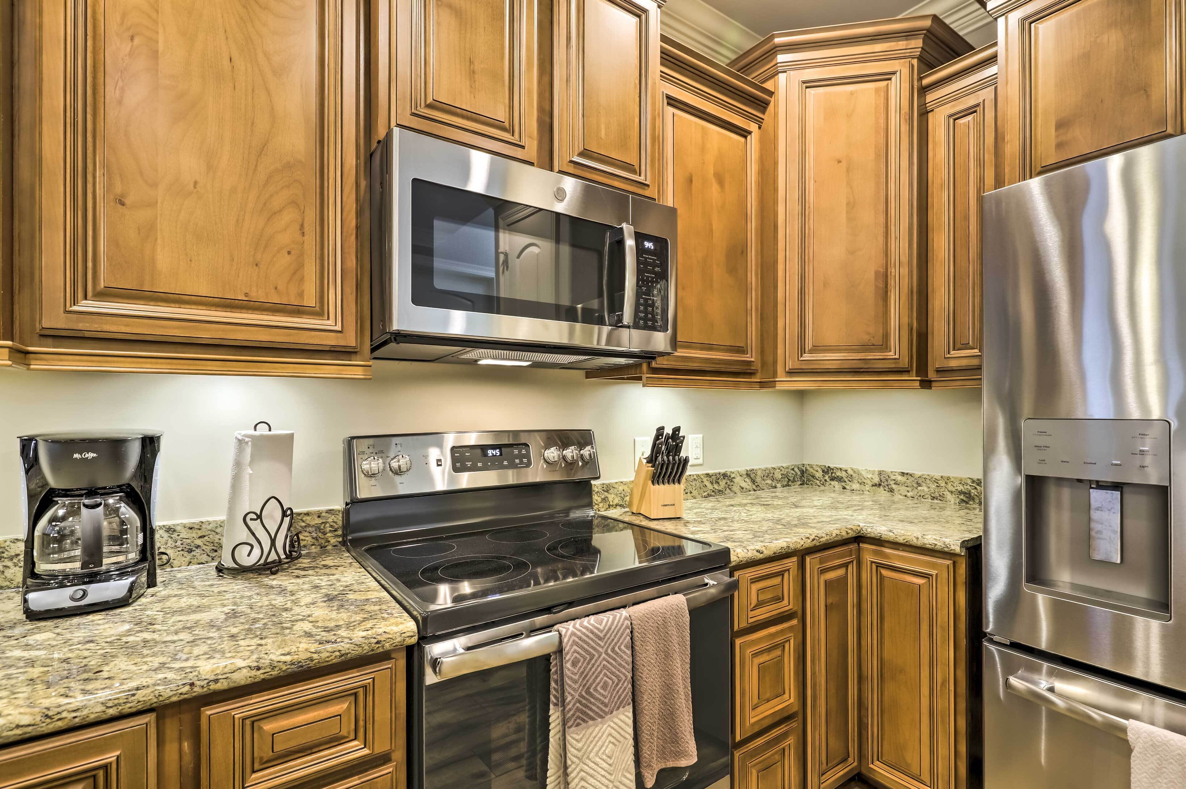 A kitchen with wooden cabinets, stainless steel appliances including a microwave, stove, and refrigerator, a granite countertop, and a coffee maker.