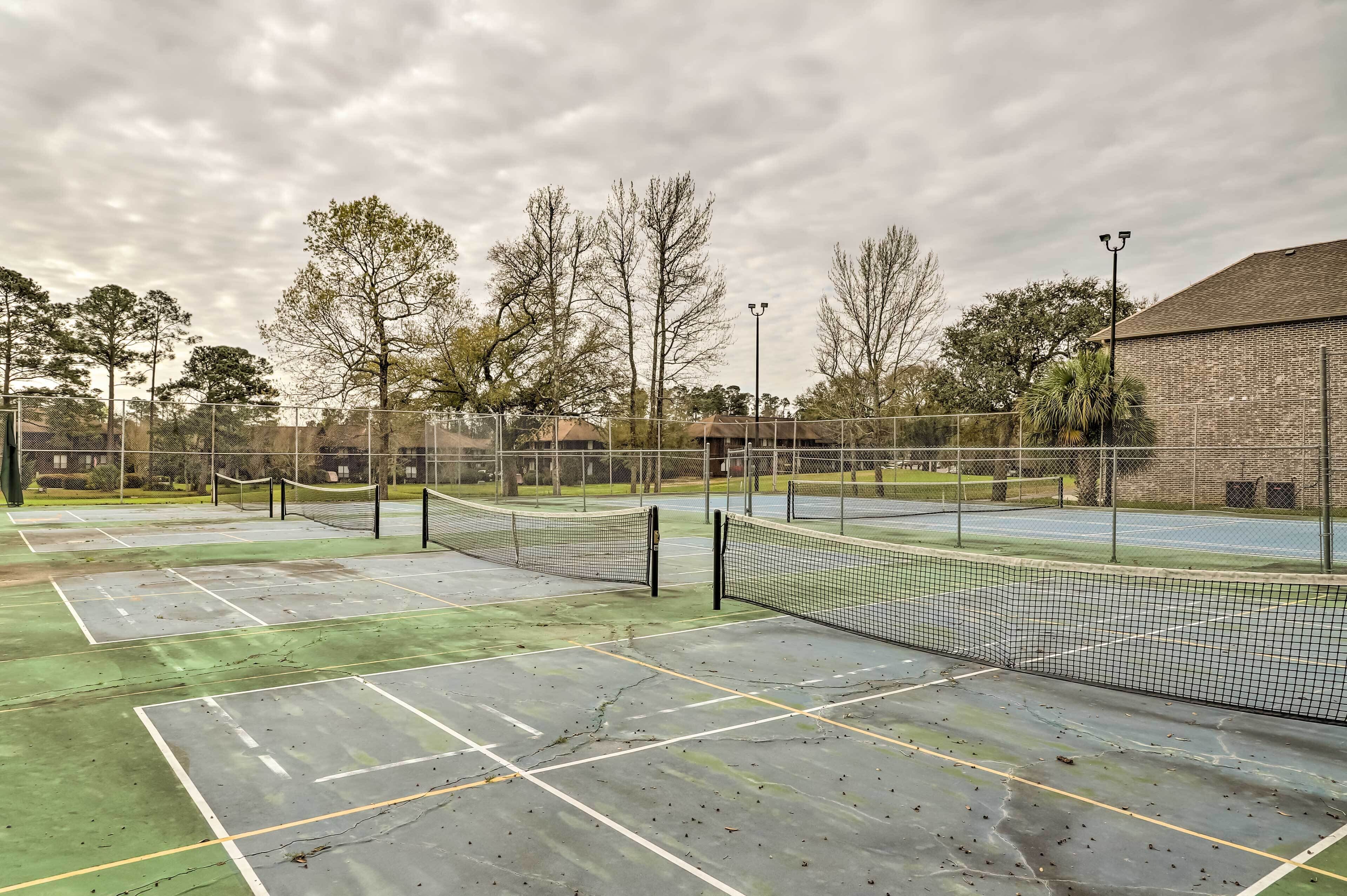 A tennis court with multiple courts, a fence, and trees in the background.