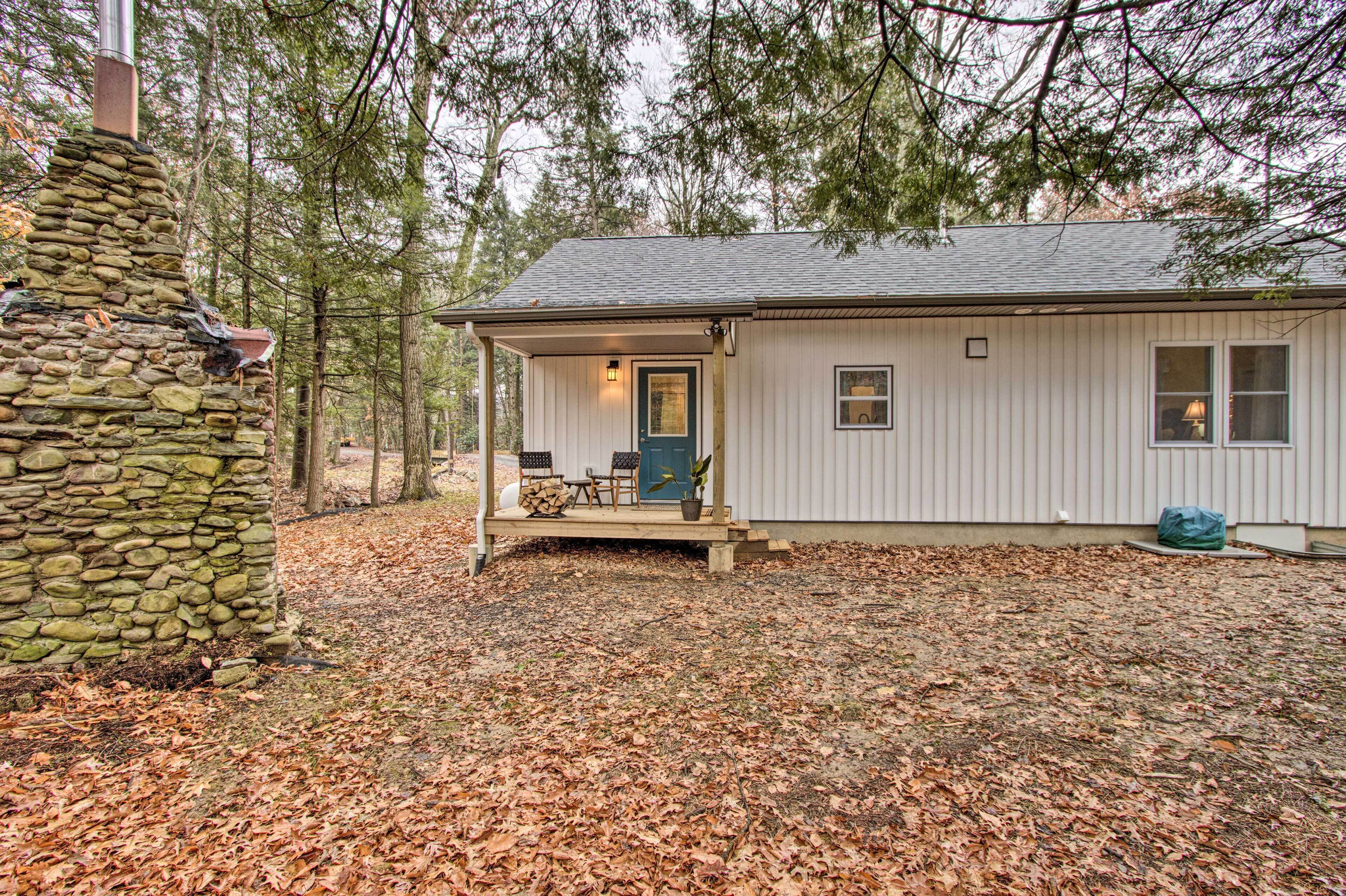 A cabin with a stone chimney, a porch with chairs, and a door with a window.