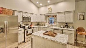 A modern kitchen with white cabinetry, stainless steel appliances, and a marble countertop island.