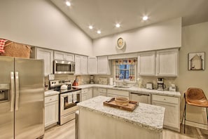 A modern kitchen with white cabinetry, stainless steel appliances, and a marble countertop island.