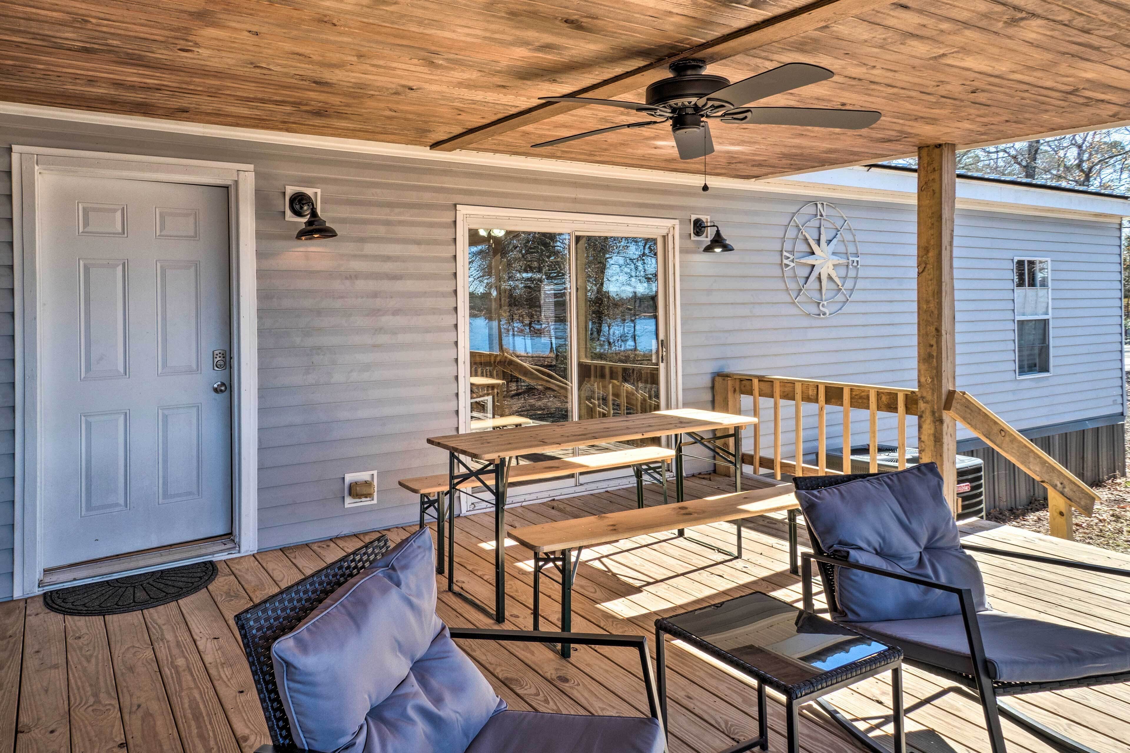 A covered deck with wooden furniture, including benches and chairs, and a ceiling fan.