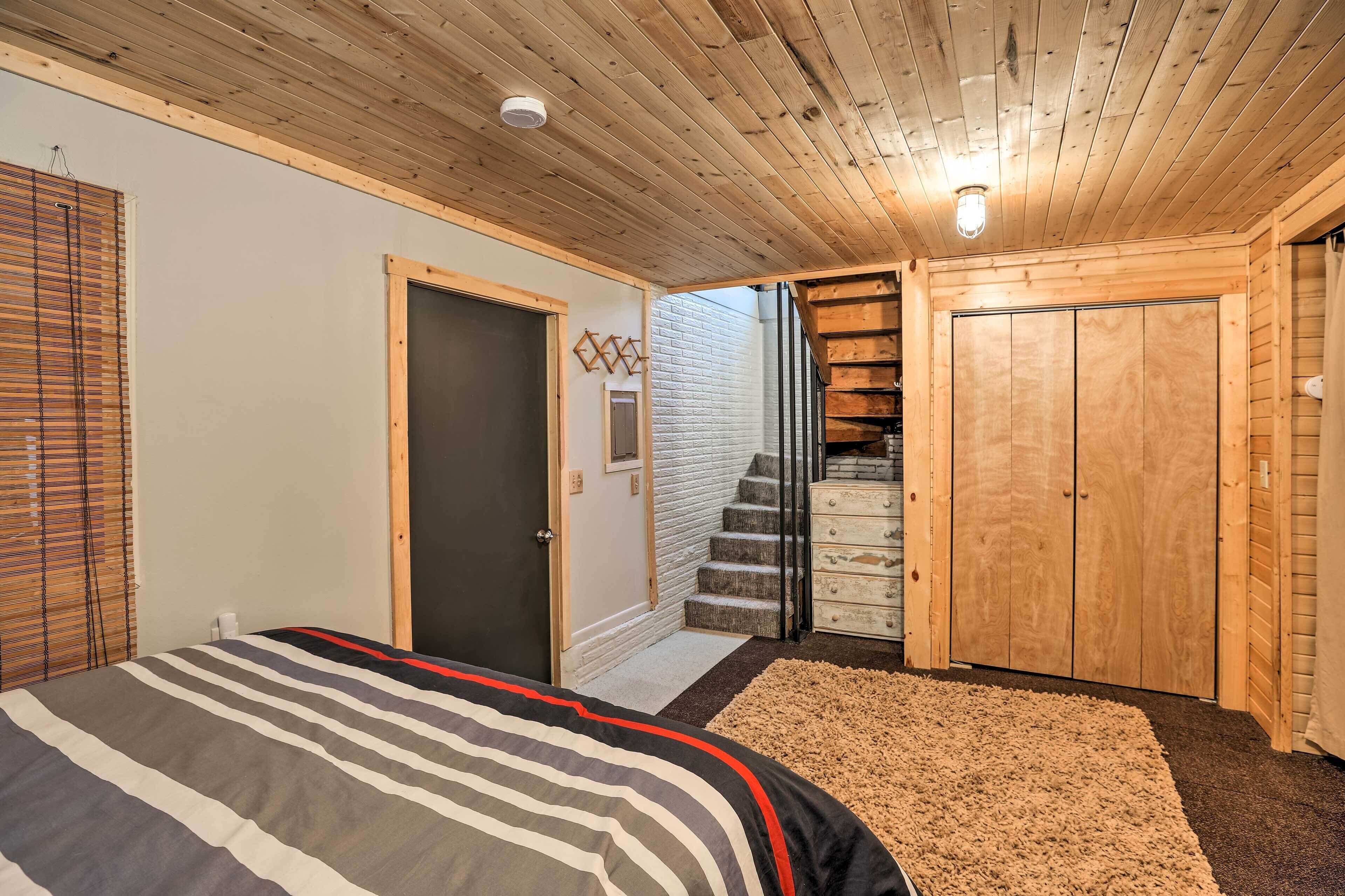 A bedroom with a bed, a wooden ceiling, a staircase, and a wardrobe.