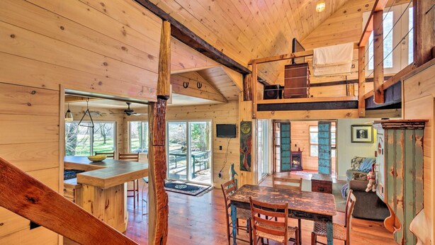 A wooden cabin interior with a dining area, a loft bedroom, and a view of the outdoors.