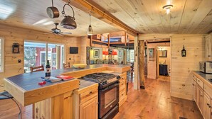 A wooden cabin kitchen with a central island, stove, and hanging lights.