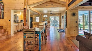 A spacious wooden interior with a dining area, kitchen, and large windows offering views of the outdoors.