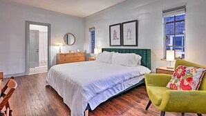 Un dormitorio con una cama grande, un sillón verde, un aparador y dos obras de arte enmarcadas en la pared.