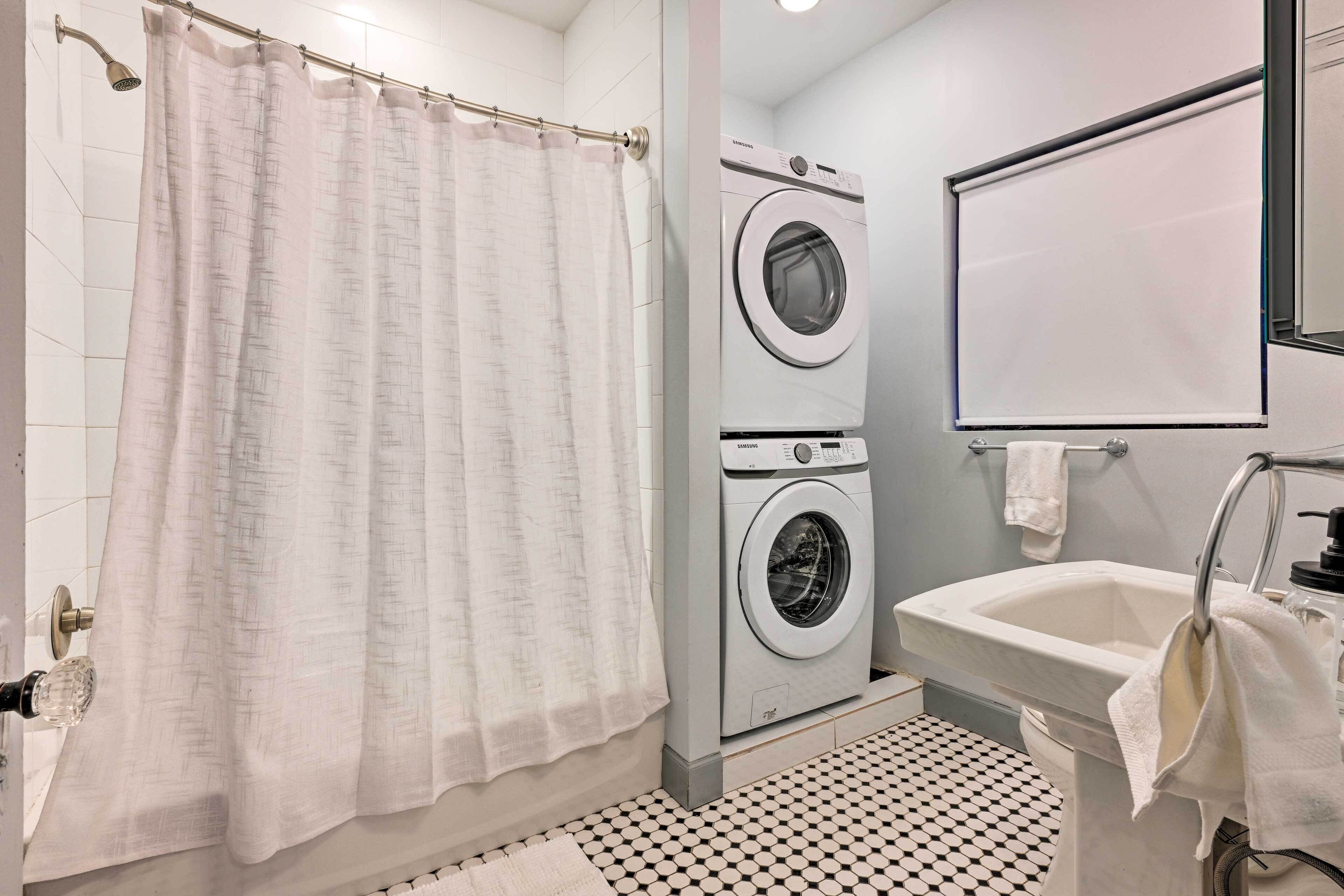 A modern bathroom with a shower, two stacked washing machines, a sink, and a mirror.
