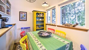 A dining area with a green tablecloth, a yellow bookshelf, and a window with a view of trees. - Dreamy Waterfront Studio w/ Hood Canal Views (Shelton)