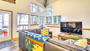 A living room with a sofa, a television, and large windows. - Dreamy Waterfront Studio w/ Hood Canal Views (Shelton)