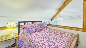 A bedroom with a sloped ceiling, a bed with floral bedding, a bedside table with a lamp, and a window with blinds. - Dreamy Waterfront Studio w/ Hood Canal Views (Shelton)
