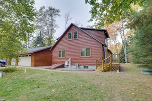 A two-story wooden cabin with a garage, a small porch, and a staircase leading to the upper floor. - Elcho Escape w/ Private Dock on Post Lake! (Elcho)