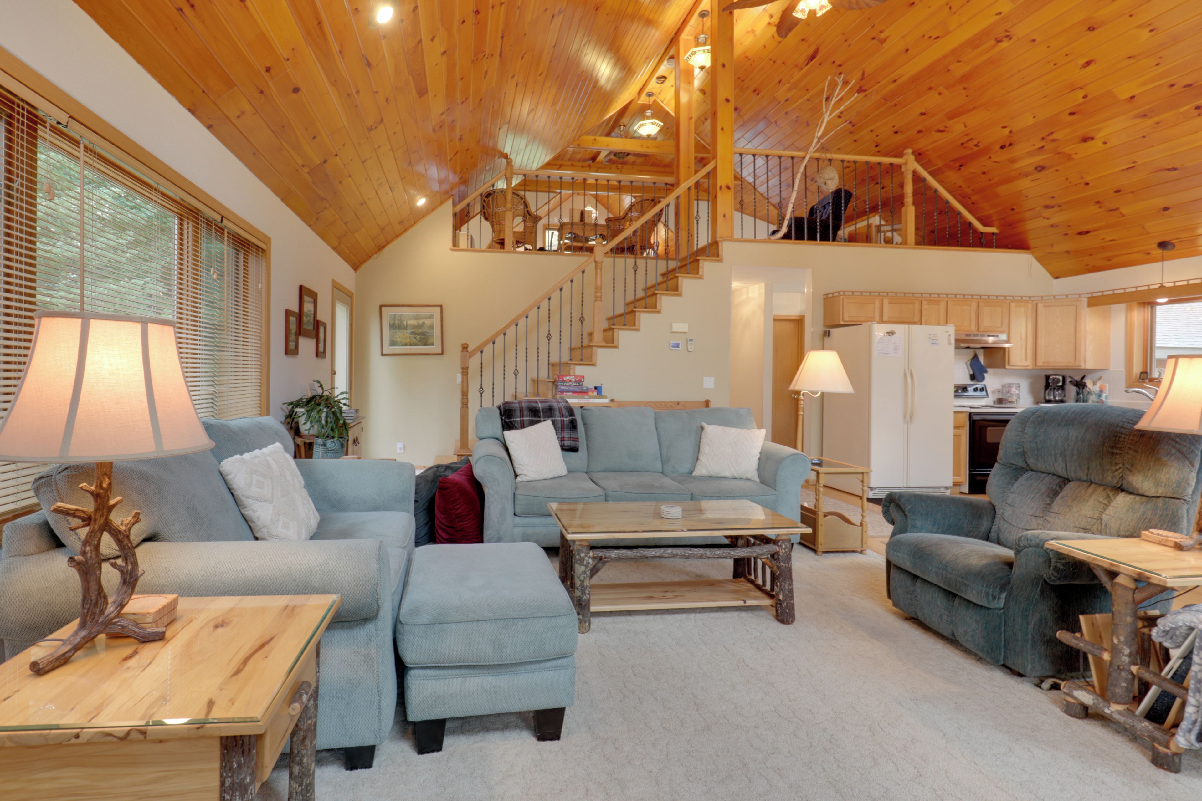 A spacious living area with a high wooden ceiling, a staircase leading to an upper level, and a kitchen area.