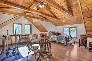 A spacious attic bedroom with a sloped ceiling, wooden beams, a bed with a plaid bedspread, a desk with a chair, and a workout area with a bench and exercise equipment. - Elcho Escape w/ Private Dock on Post Lake! (Elcho)