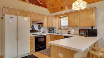 A modern kitchen with wooden cabinets, a central island, a refrigerator, stove, microwave, and a hanging light fixture.
