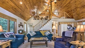 A spacious living room with a high wooden ceiling, a staircase leading to an upper level, and a kitchen area visible through an open door. - Elcho Escape w/ Private Dock on Post Lake! (Elcho)