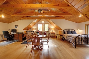 A spacious attic bedroom with a wooden ceiling, a bed, a desk, and a dining area. - Elcho Escape w/ Private Dock on Post Lake! (Elcho)
