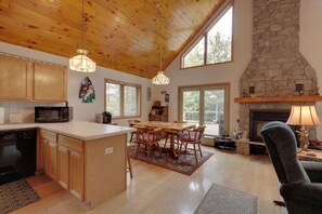 A spacious kitchen with wooden cabinets, a central island, and a stone fireplace. - Elcho Escape w/ Private Dock on Post Lake! (Elcho)