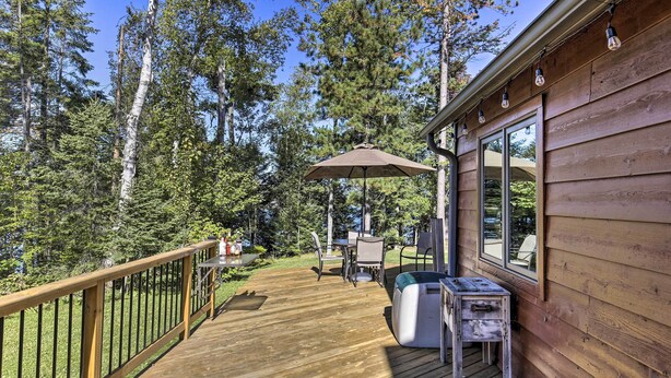 A wooden deck with a table and chairs, a small table with a lamp, and a large umbrella. - Elcho Escape w/ Private Dock on Post Lake! (Elcho)