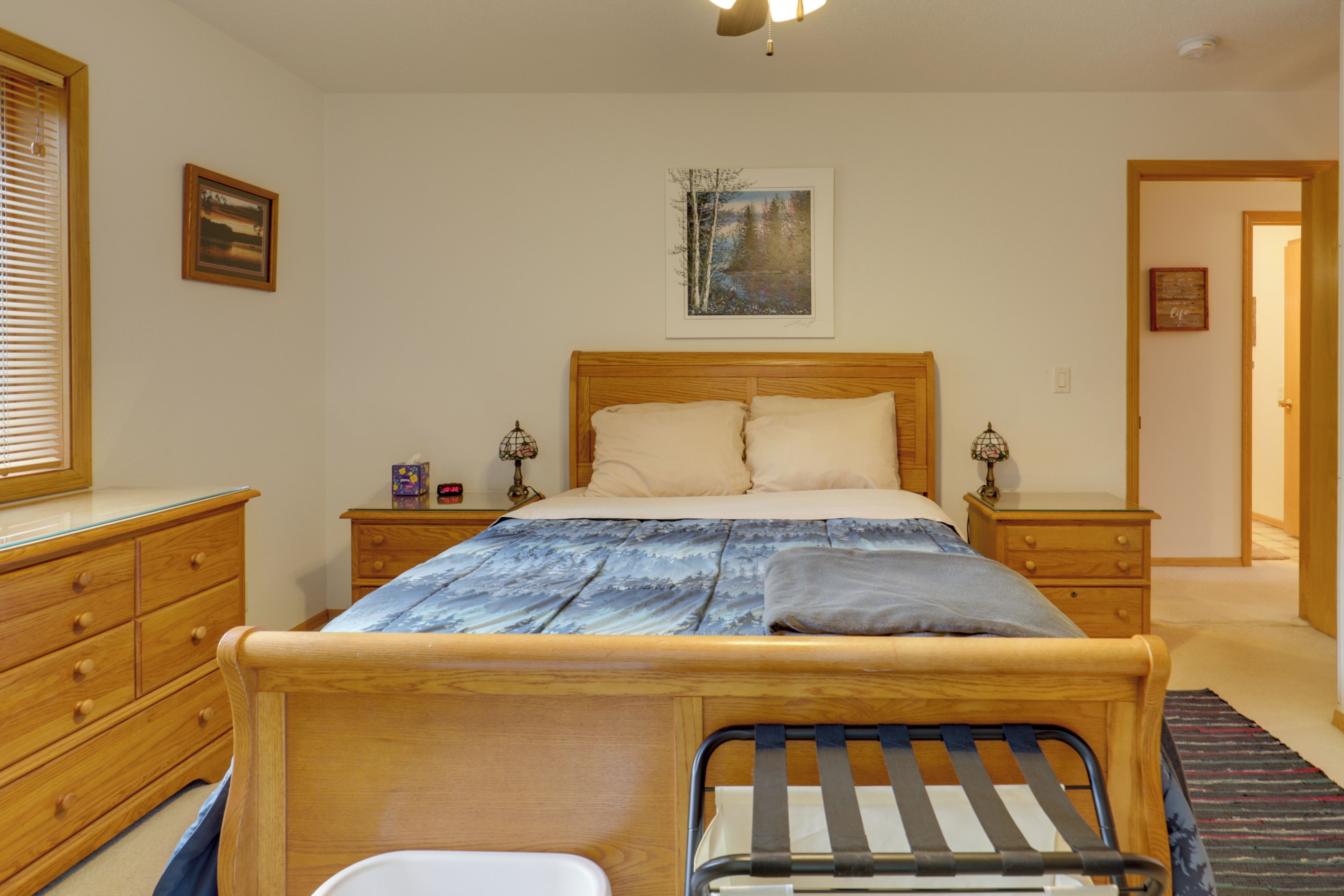 A bedroom with a wooden bed, bedside tables, a nightstand, a dresser, and a painting on the wall.