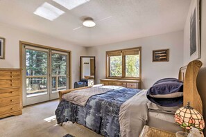 Une chambre à coucher avec un grand lit, une commode, un bureau et une fenêtre donnant sur les arbres.
