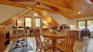 A spacious attic bedroom with a wooden ceiling, a large window, a bed, and a dining table with chairs.