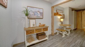 Un couloir avec une console blanche, un tableau encadré et une plante en pot. On y trouve également un banc en bois et une petite table avec une lampe.