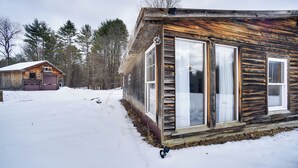 Une cabane en bois dotée de grandes fenêtres et d’un garage, entourée de neige et d’arbres.