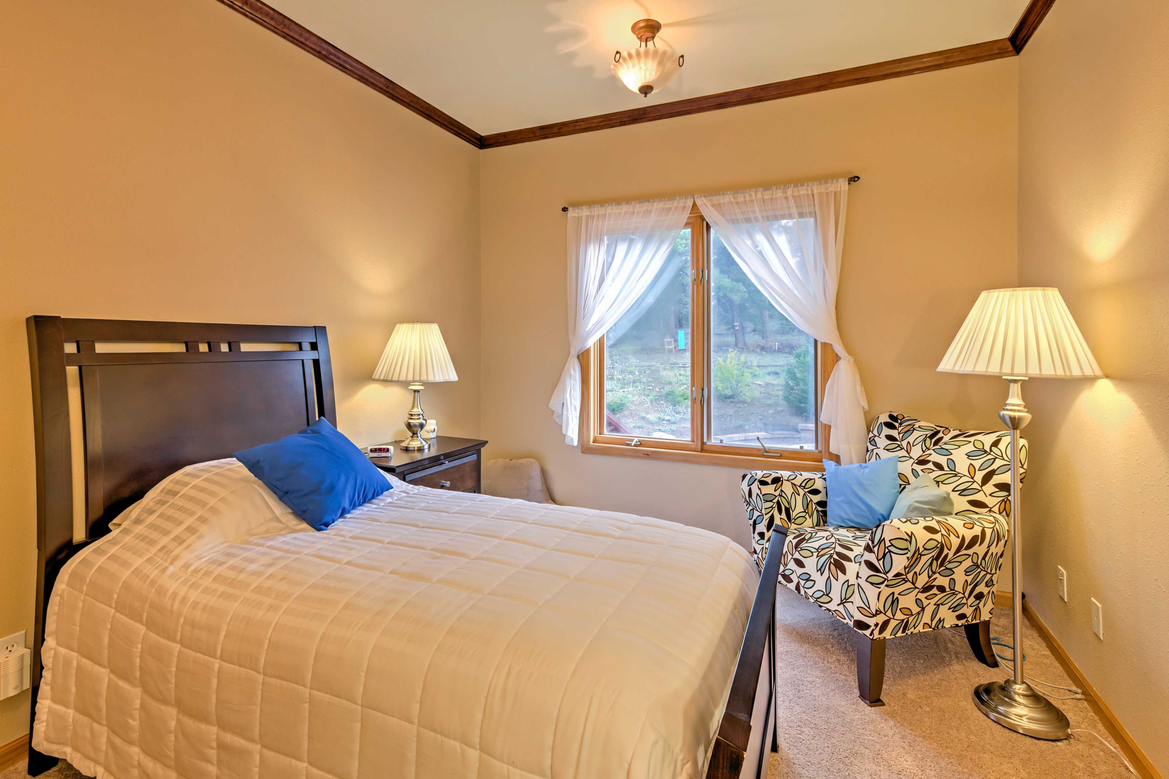 A bedroom with a large bed, two bedside lamps, a patterned armchair, and a window with sheer curtains.