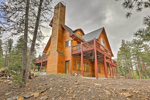 A large wooden cabin with a prominent chimney, a covered porch, and a rustic setting surrounded by trees.