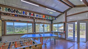 A room with a foosball table, ping pong table, and a variety of hats displayed on shelves. - Two Cozy Medina Cottages, Game Room, Mountain View (Medina)