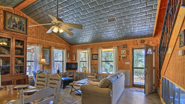 A cozy cabin interior with a dining area, a sofa, a ceiling fan, and large windows. - Two Cozy Medina Cottages, Game Room, Mountain View (Medina)