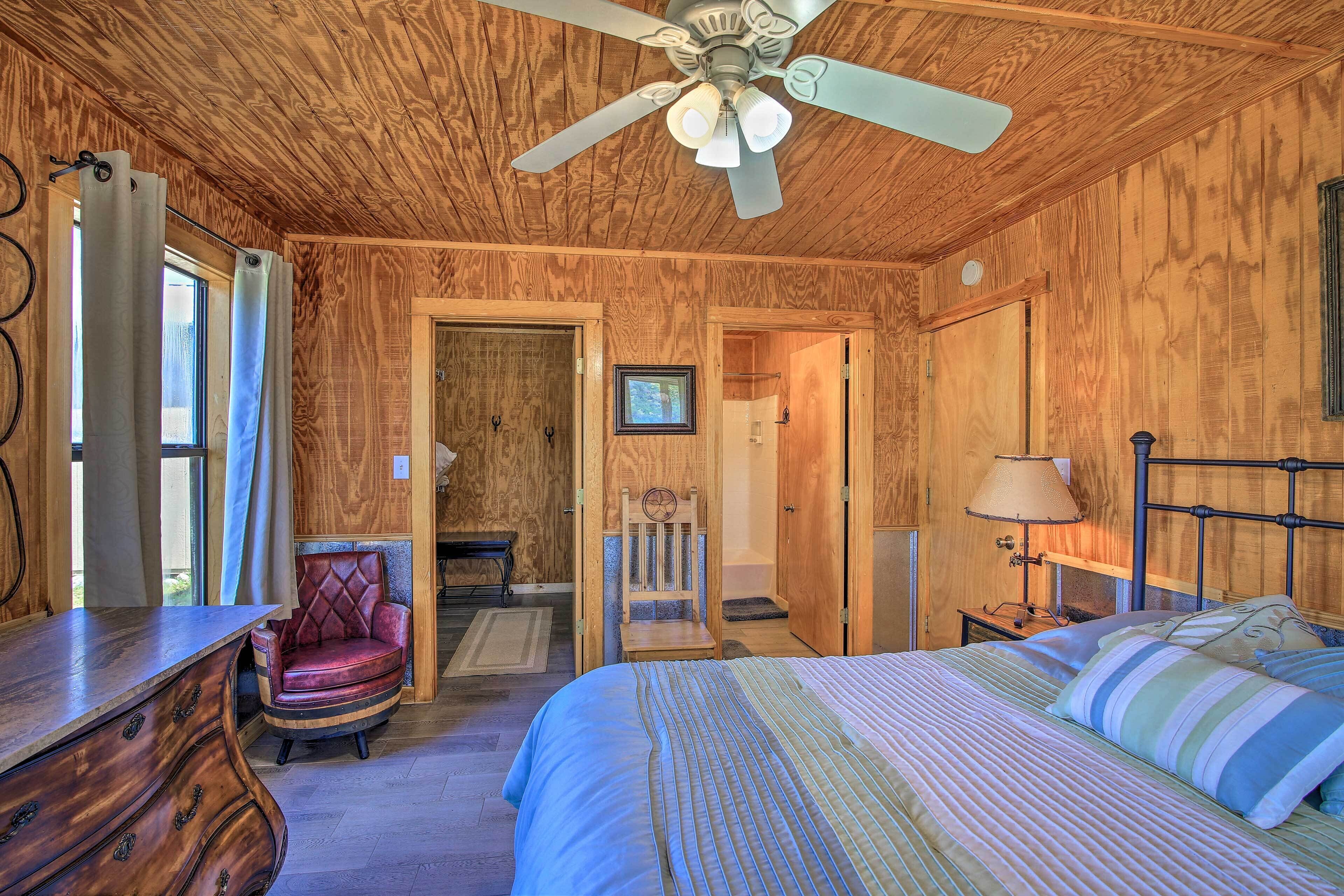 A wooden-paneled room with a bed, a chair, a desk, and a ceiling fan.