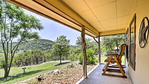 A covered patio with a view of a landscaped garden and hills. There are wooden benches and a table under the shelter. - Two Cozy Medina Cottages, Game Room, Mountain View (Medina)