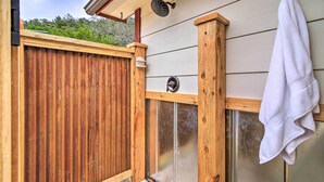 A wooden deck with a glass door, a towel hanging on a hook, and a showerhead above. - Two Cozy Medina Cottages, Game Room, Mountain View (Medina)