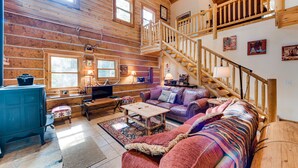 Ein gemütliches Blockhaus-Interieur mit einer Holztreppe, einer Couch, einem Couchtisch und einem Fernseher.